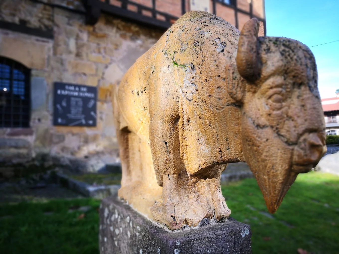 Primer plano lateral de la cabeza y el lomo de El Bisonte de Jesús Otero con una fachada entramada al fondo