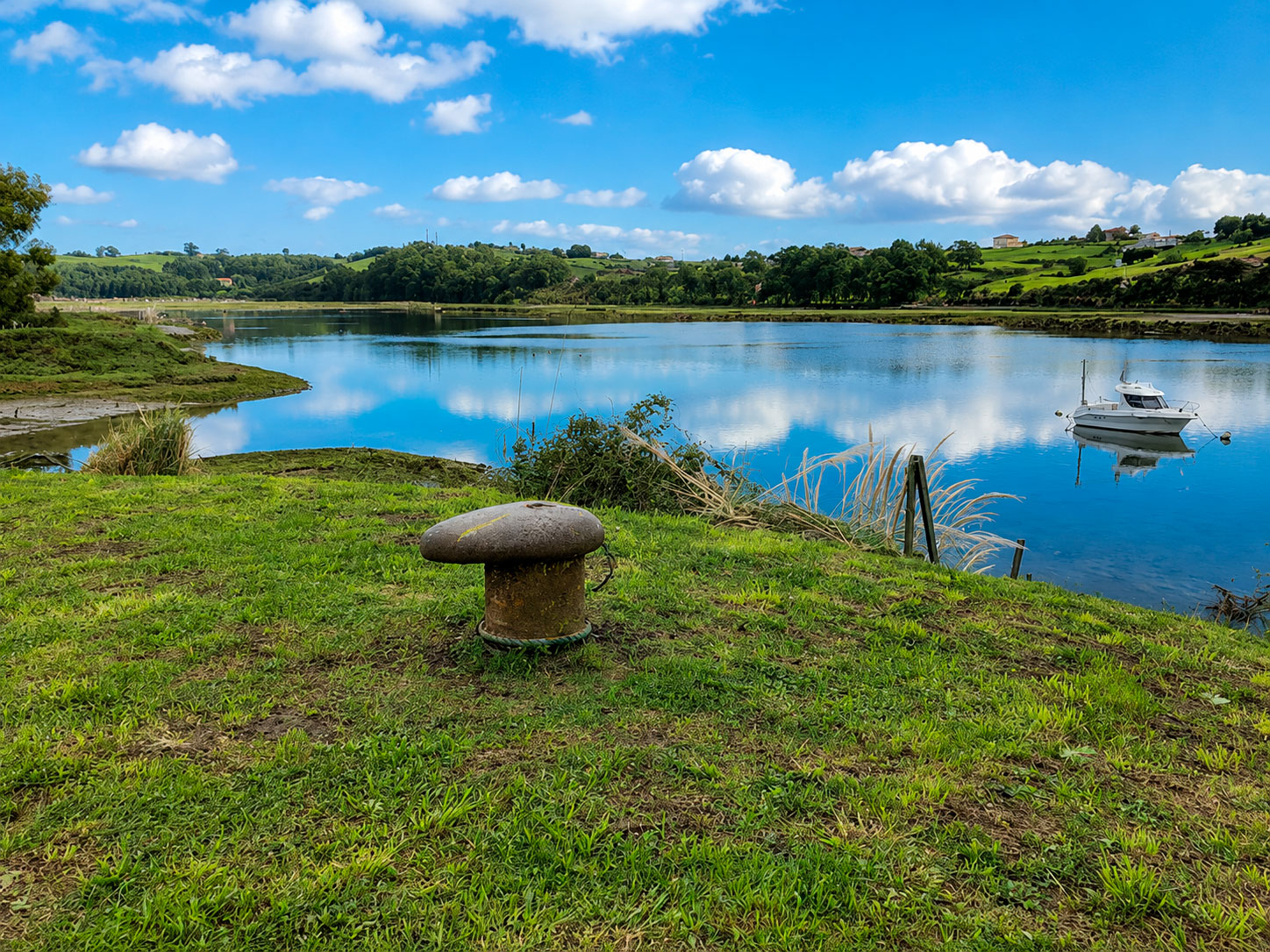 Bolardo de amarre junto a la ría de San Martín de la Arena en Los Cantos, con aguas tranquilas y marisma al fondo