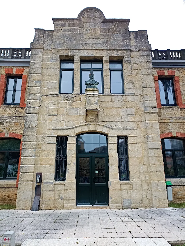 Cuerpo central de la fachada del Antiguo Colegio de San José en Suances, con el busto de Juan José Gómez Quintana bajo los ventanales seriados y el remate del hastial