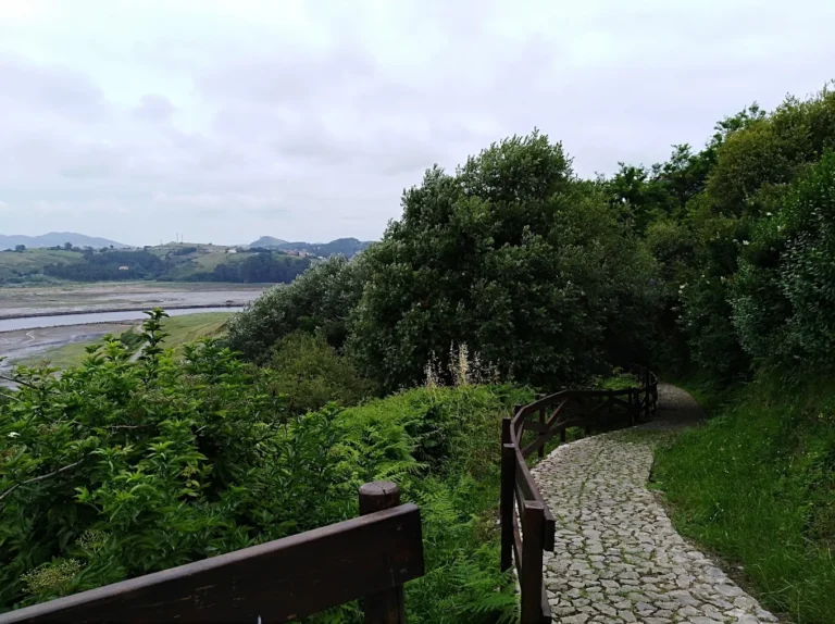 Camino empedrado con barandilla de madera del Atajo de la Fuente de Enmedio en Suances, con la ría de San Martín de la Arena al fondo