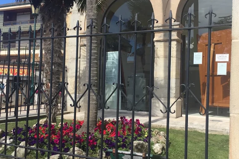 Detalle de dos arcadas del soportal del Ayuntamiento de Suances a pie de calle, tras la verja de forja y las jardineras de flores