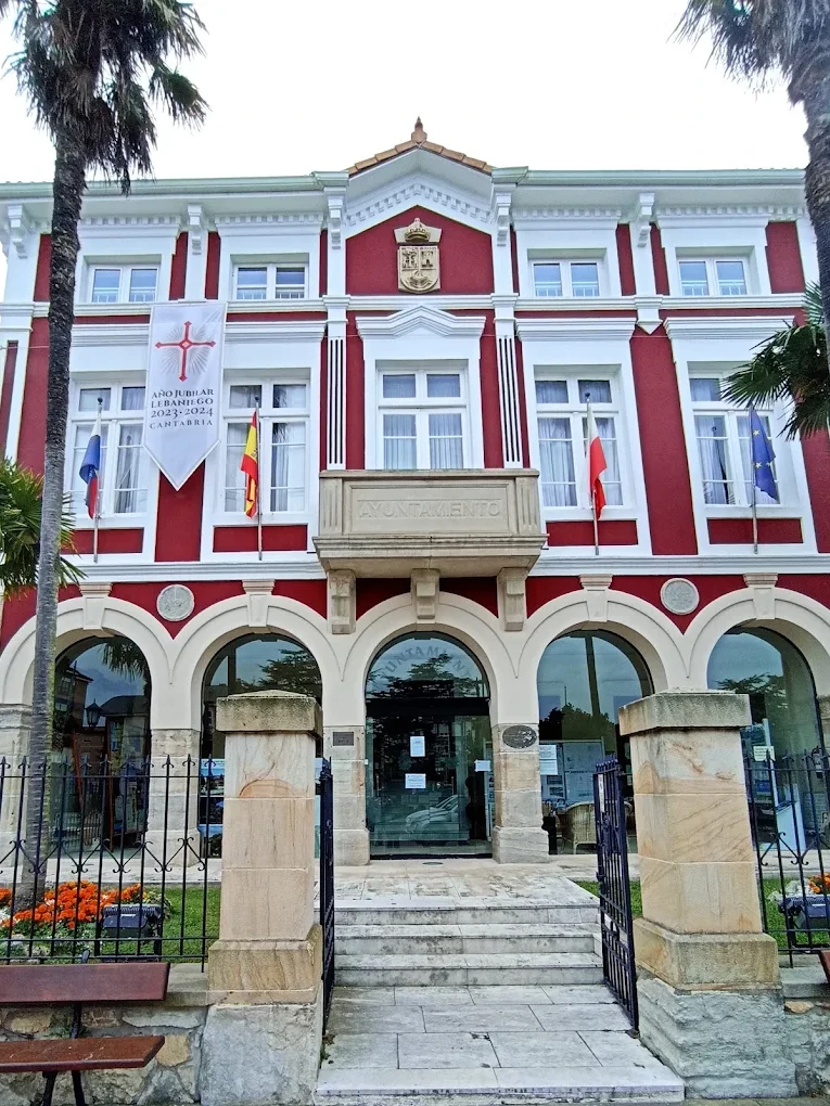 Fachada principal del Ayuntamiento de Suances en la plaza de Viares, con las cinco arcadas acristaladas, el balcón y el escudo municipal en tonos rojo y blanco