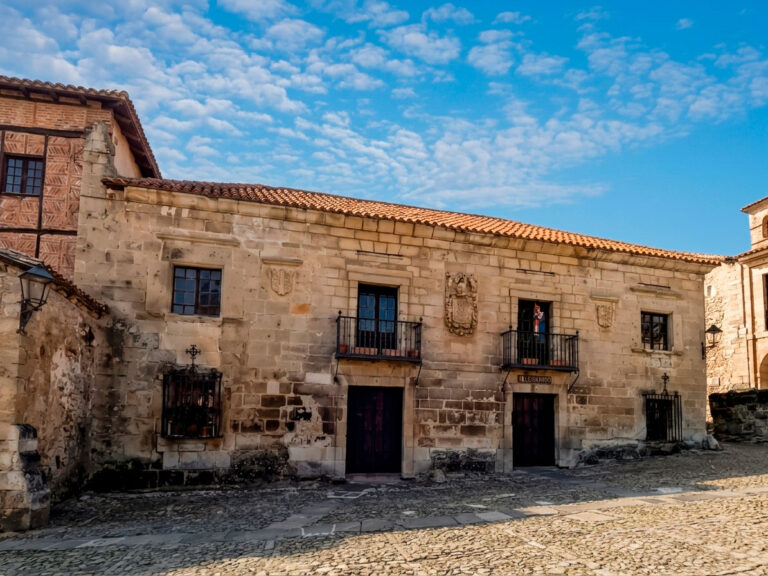Fachada de piedra de la Casa de la Archiduquesa o de los Abades en Santillana del Mar, con dos puertas simétricas, dos balcones de hierro y varios escudos labrados por Jesús Otero