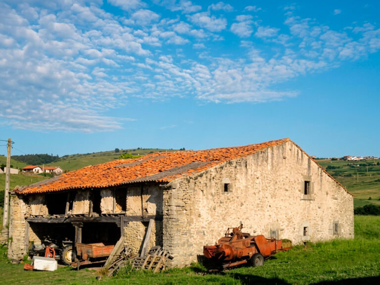 Casa de los Arce en Hinojedo (Suances), casa de labranza del siglo XVII con muros de entramado de madera y mampostería, y maquinaria agrícola antigua junto a la fachada