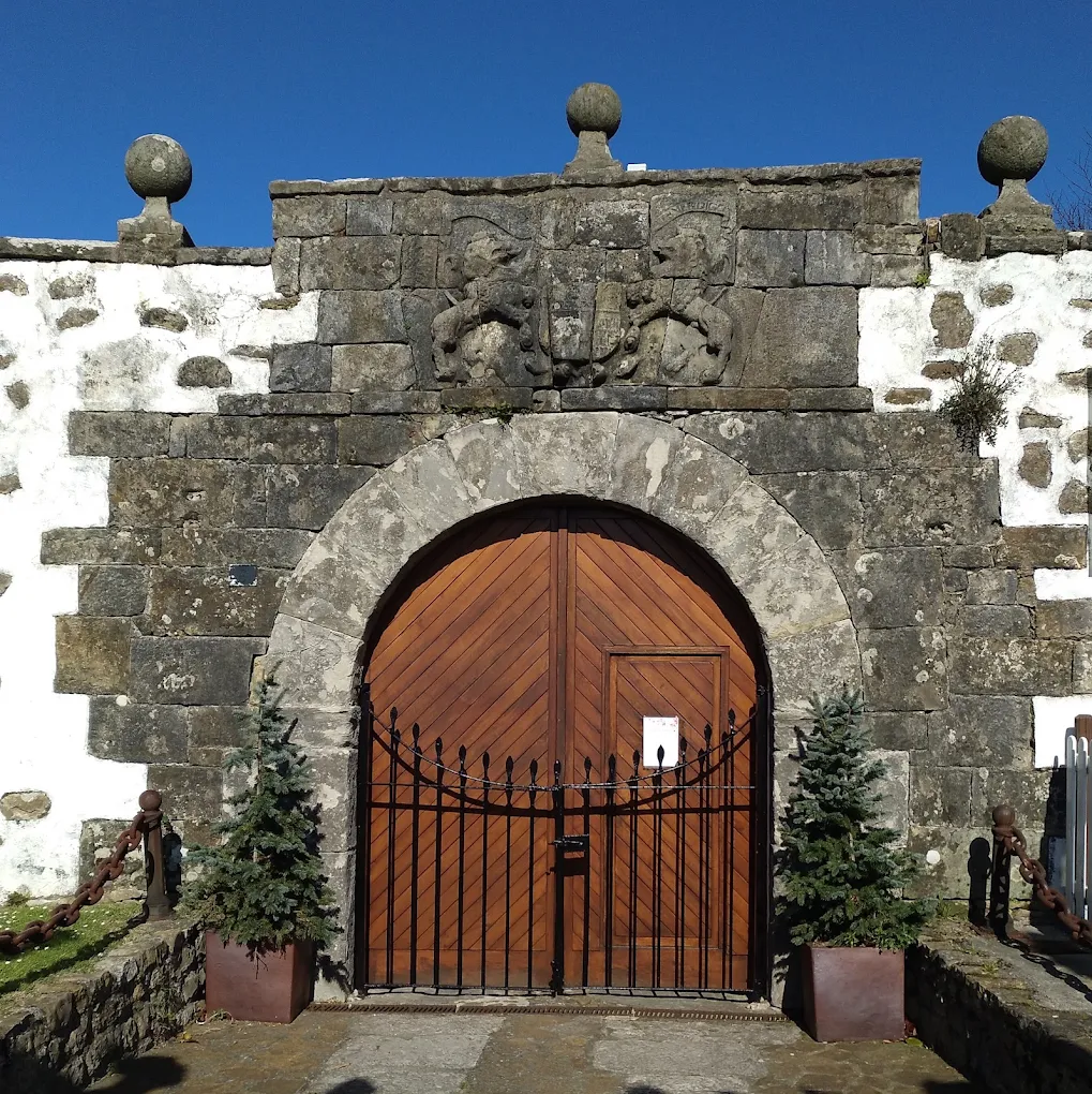 Portalada de la Casa de los Polanco en Suances, con arco de medio punto, escudo cuartelado sostenido por dos leones y tres bolas de piedra rematando el muro