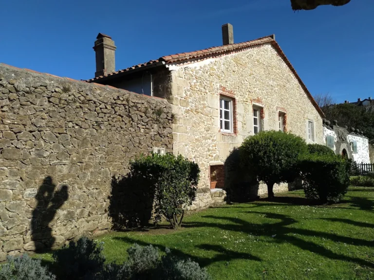 Fachada de piedra de la Casa de los Polanco en Suances, con vanos de distintos tamaños y la portalada asomando al fondo tras el jardín