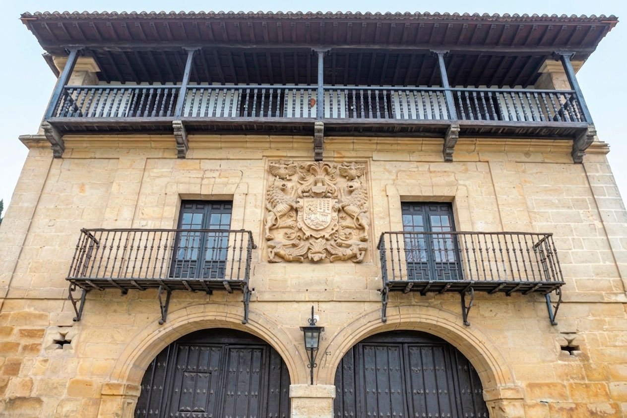 Vista actual en contrapicado de la Casona de los Tagle en Santillana del Mar, con la galería de madera, el escudo cuartelado y los dos arcos de acceso