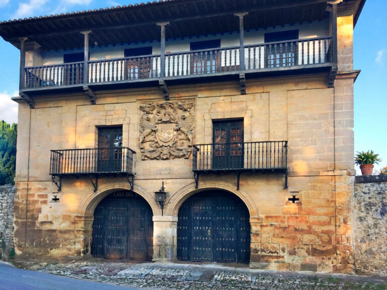 Fachada principal de la Casona de los Tagle en Santillana del Mar, con dos arcos de acceso, balcones de forja y el gran escudo cuartelado bajo la galería