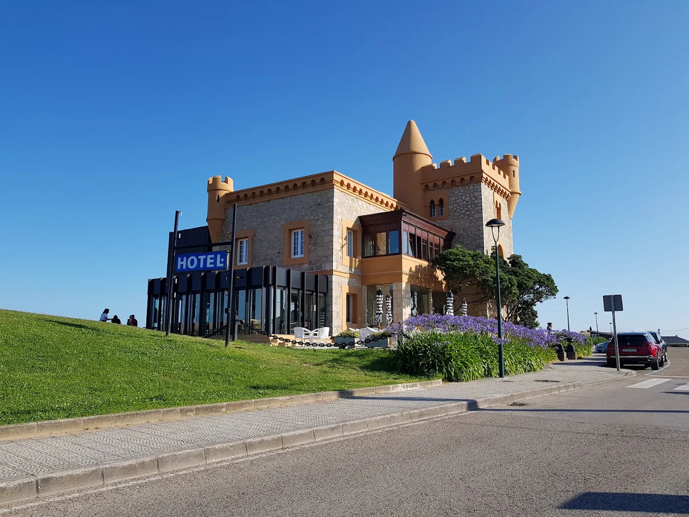 Vista actual del castillo de Ceruti desde el paseo, con el letrero del hotel y agapantos en flor en primer término