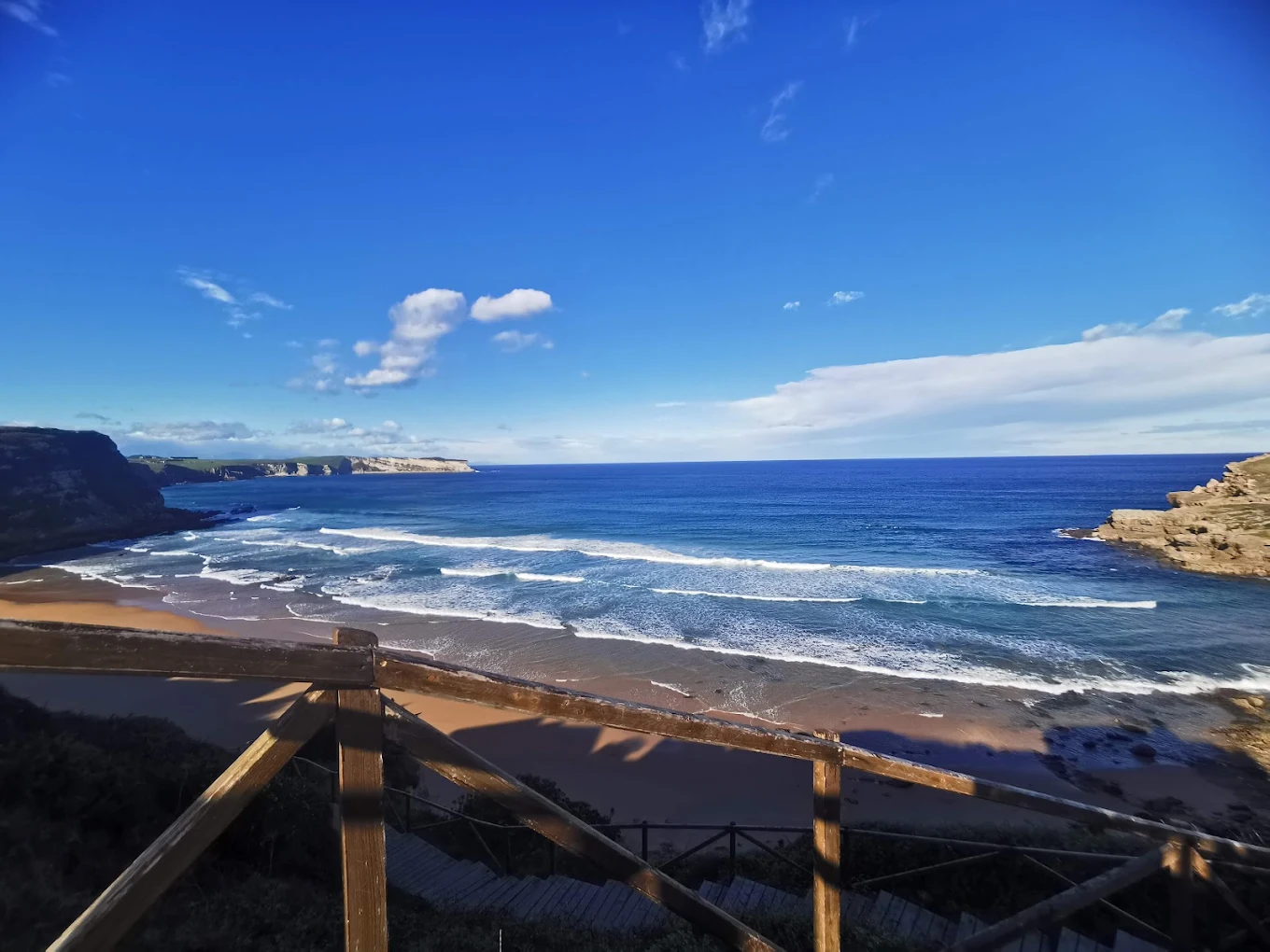 Vista de la playa y el acantilado de Suances desde el mirador junto al castillo de Ceruti, con el oleaje rompiendo en la orilla