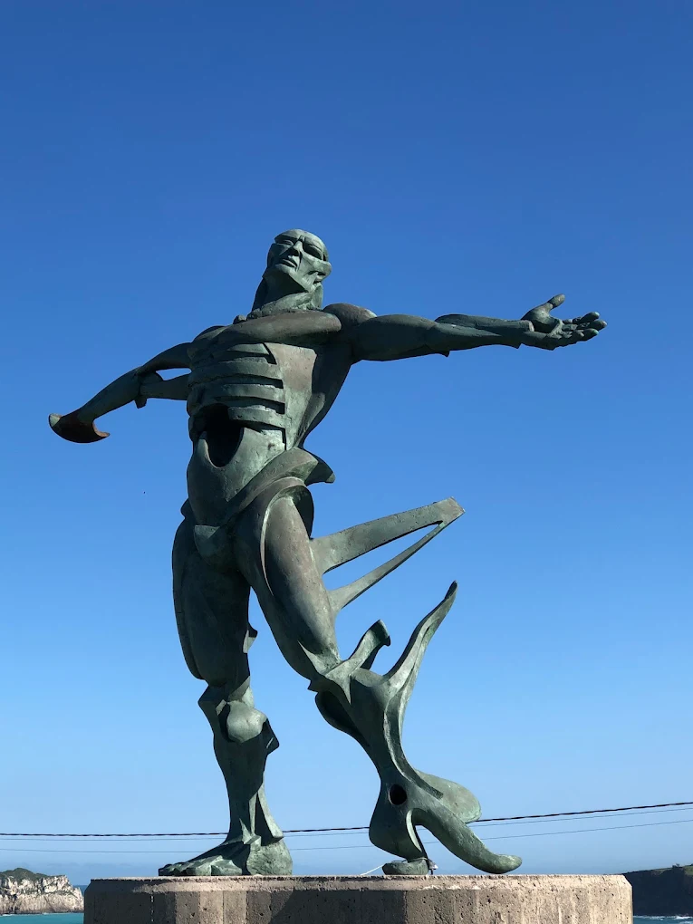 Escultura El Hombre de los Vientos en Suances, figura de bronce con los brazos abiertos sobre fondo de cielo azul