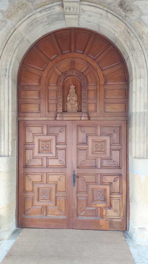 Puerta principal de madera de la iglesia de Nuestra Señora de las Lindes de Suances, con la talla de la Virgen sobre el dintel