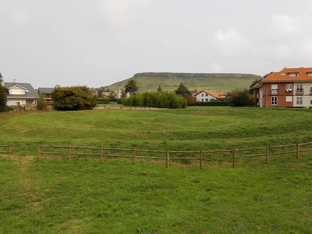 Vista a pie de campo de los relieves de tierra de la Mota de Trespalacios en Hinojedo, con el vallado de madera que rodea el foso