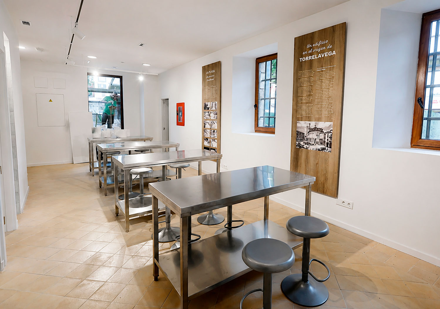Sala de talleres del Museo del Hojaldre de Torrelavega con mesas de acero y paneles sobre la historia del edificio