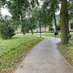 Parque de La Ribera (Suances): el paisajístico junto a la ría Sendero de hormigón serpenteando entre árboles y bancos en el parque de La Ribera de Suances, con el suelo mojado tras la lluvia