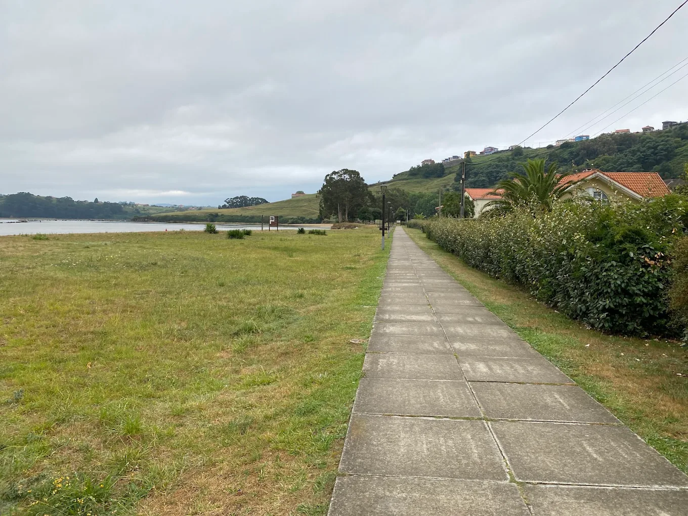 Camino de losas de hormigón junto a la ría en el parque de La Ribera, con las casas del barrio pesquero en la ladera al fondo