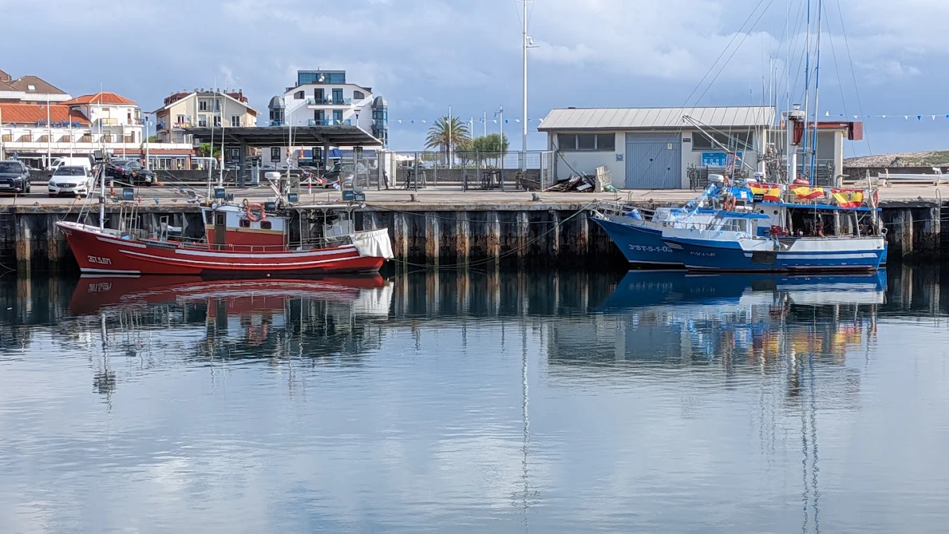 Barcos pesqueros reflejados en las aguas tranquilas del puerto de Suances junto al edificio de la lonja