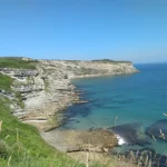 Punta Ballota (Tagle): geología, ruta y la Torre de San Telmo Acantilados escalonados de roca caliza en Punta Ballota (Tagle, Suances), con sus estratos horizontales asomando sobre una cala de aguas turquesas