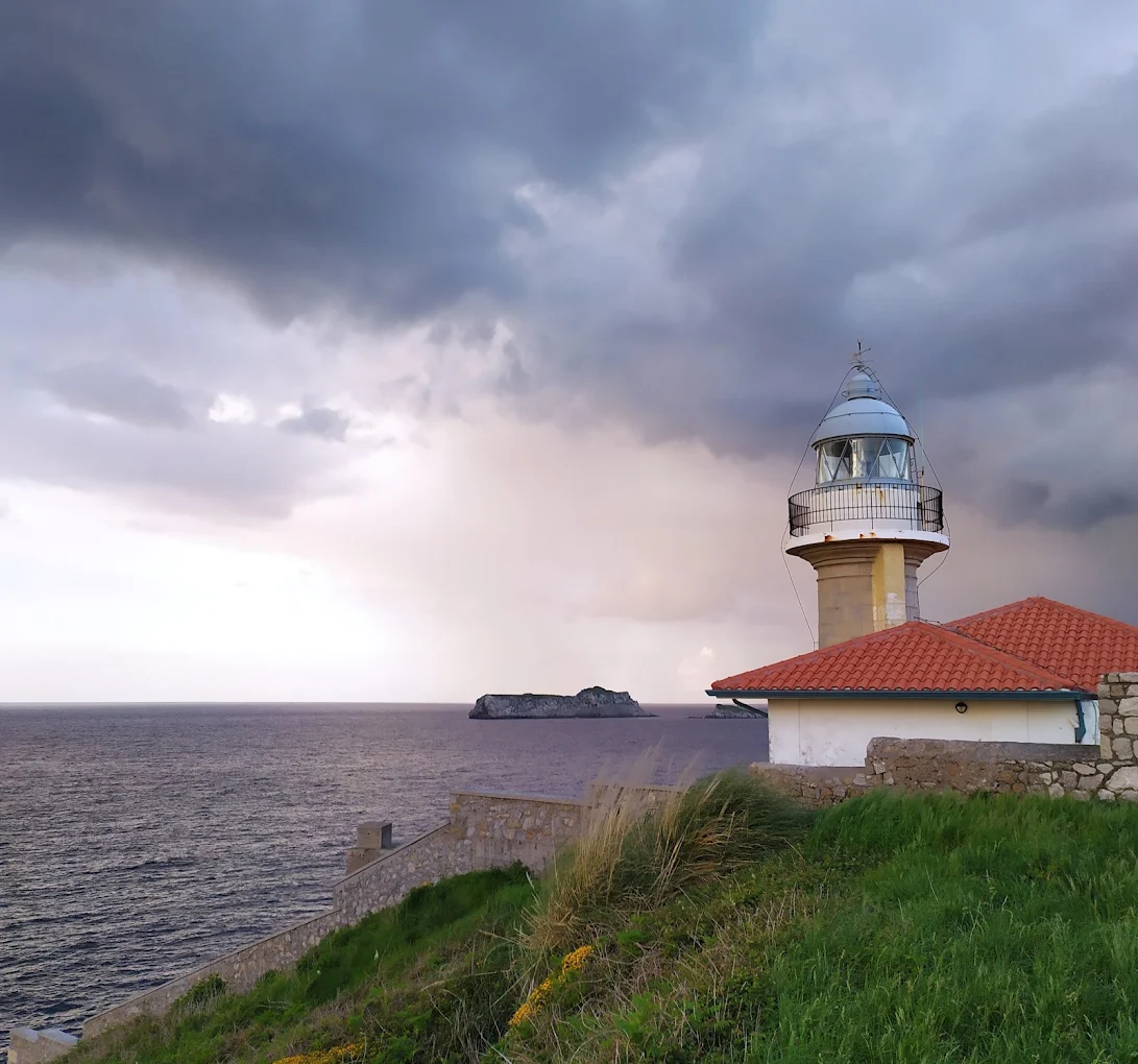 Faro de Suances bajo un cielo tormentoso con un islote al fondo