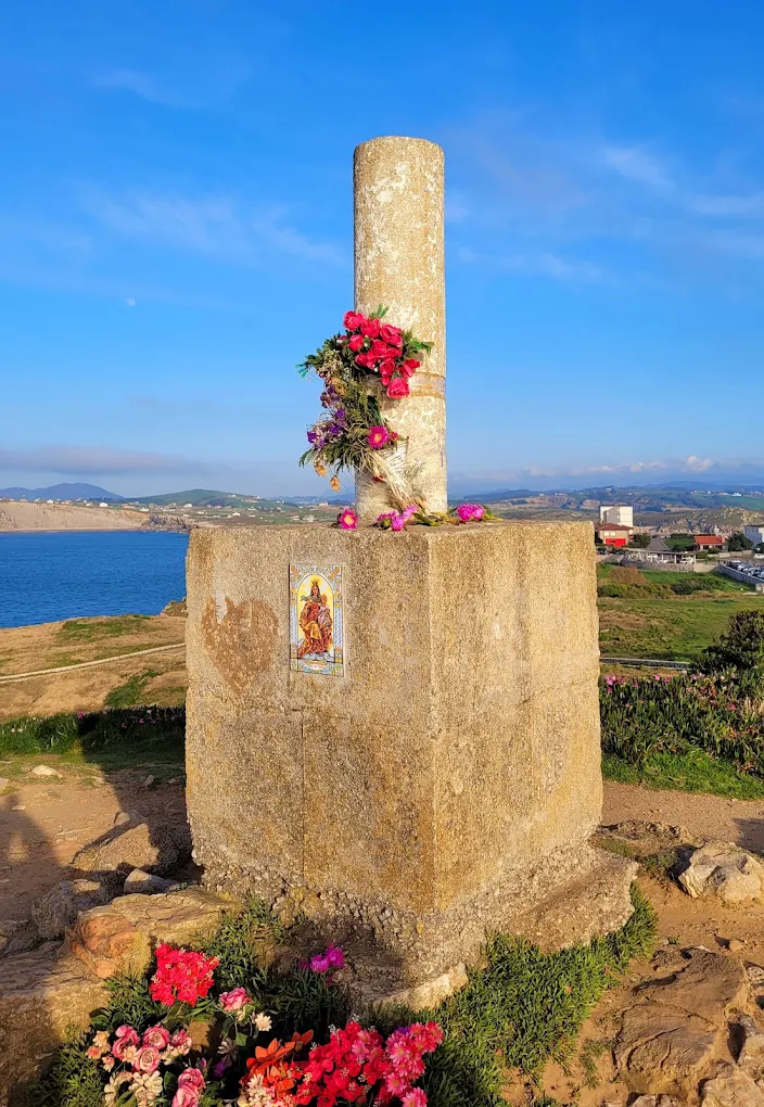 Detalle del vértice geodésico Garita con su base de hormigón, flores y vistas a la bahía de Suances