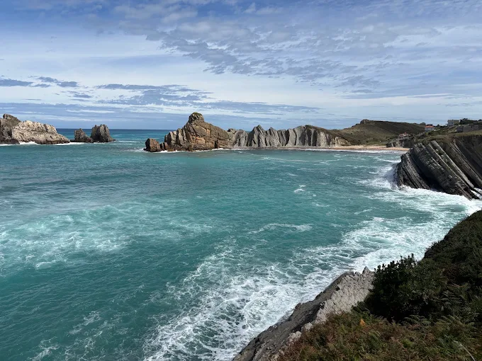 Acantilado de estratos verticales con playa de arena e islotes en el mar