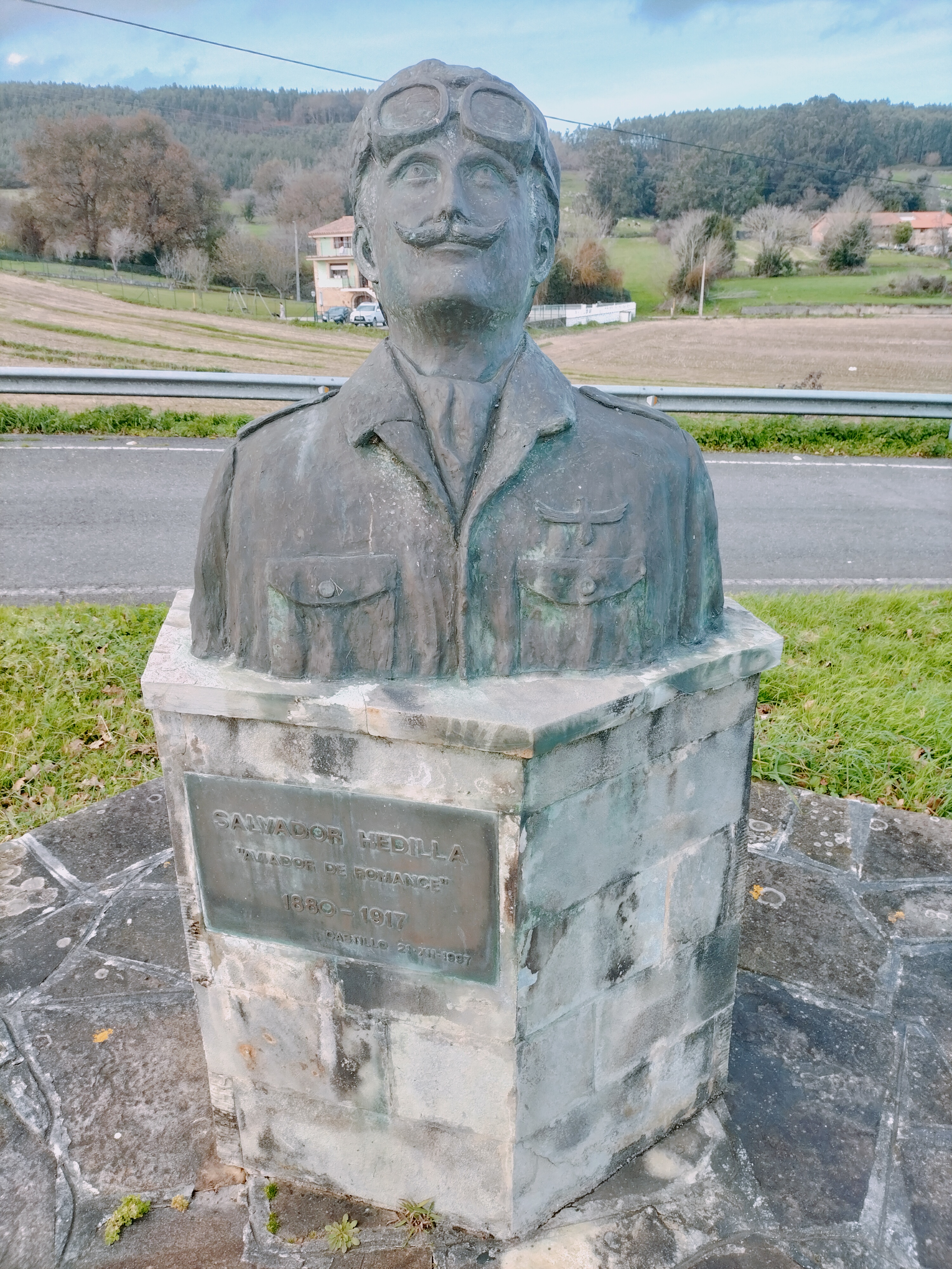 Busto de Salvador Hedilla en Castillo, Arnuero, con la placa conmemorativa y el paisaje rural detrás