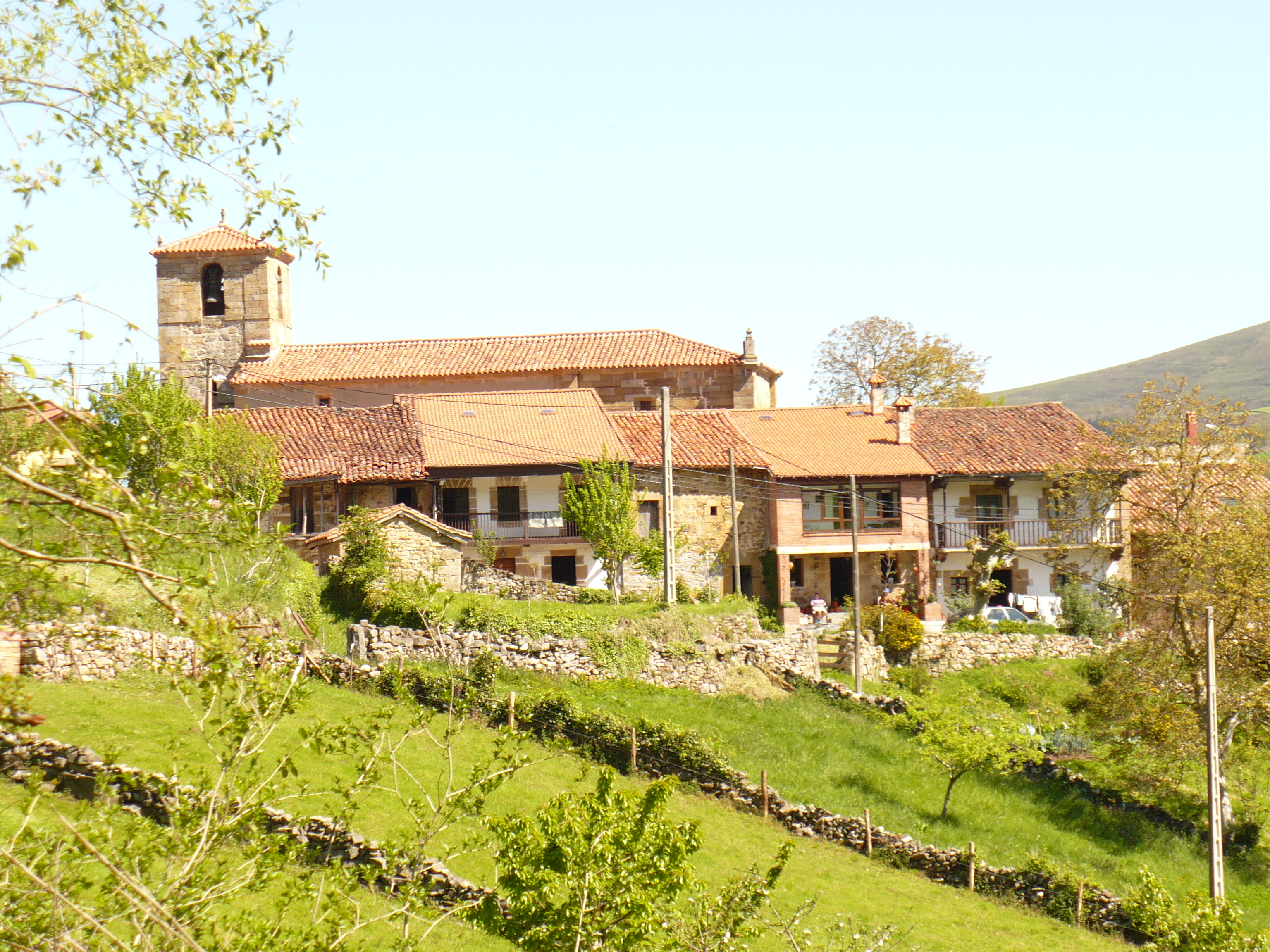 Vista de San Miguel de Luena y su iglesia entre prados y laderas